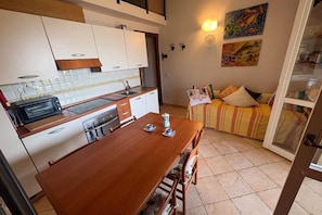 Eine kleine Küche mit Esstisch, Toaster und Spüle. Es gibt ein Sofa mit Kissen und ein Bild an der Wand.