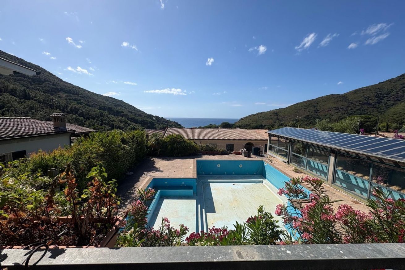 Un espace piscine offrant une vue sur la mer, entouré de verdure et bordé d’un bâtiment équipé de panneaux solaires.