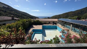 A pool area with a view of the sea, surrounded by greenery and a building with solar panels. - Callistemo Apartment (Rio)