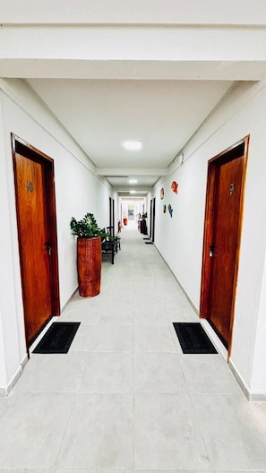 A hotel corridor with two wooden doors, a potted plant, and a tiled floor. - Porto Beach Flats Dolce Vita Piscina 03C (Ipojuca)