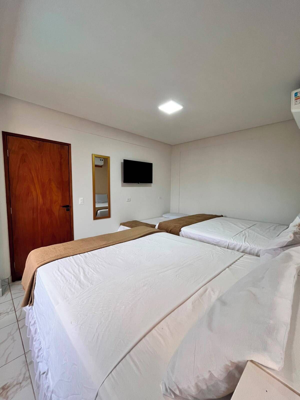 A hotel room with two beds, a wooden door, a flat-screen TV, and a ceiling light.