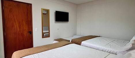 A hotel room with two beds, a wooden door, a flat-screen TV, and a ceiling light.