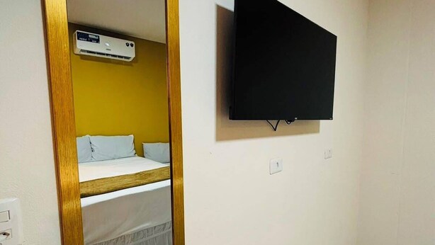 Ein Zimmer mit einem Bett, einem an der Wand befestigten Fernseher und einem Spiegel mit goldener Rahmung.