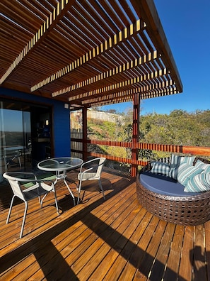 A wooden deck with a pergola, outdoor seating, and a view of the surrounding landscape.