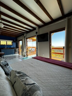 A bedroom with a large bed, a TV mounted on the wall, and a view of the outdoors.