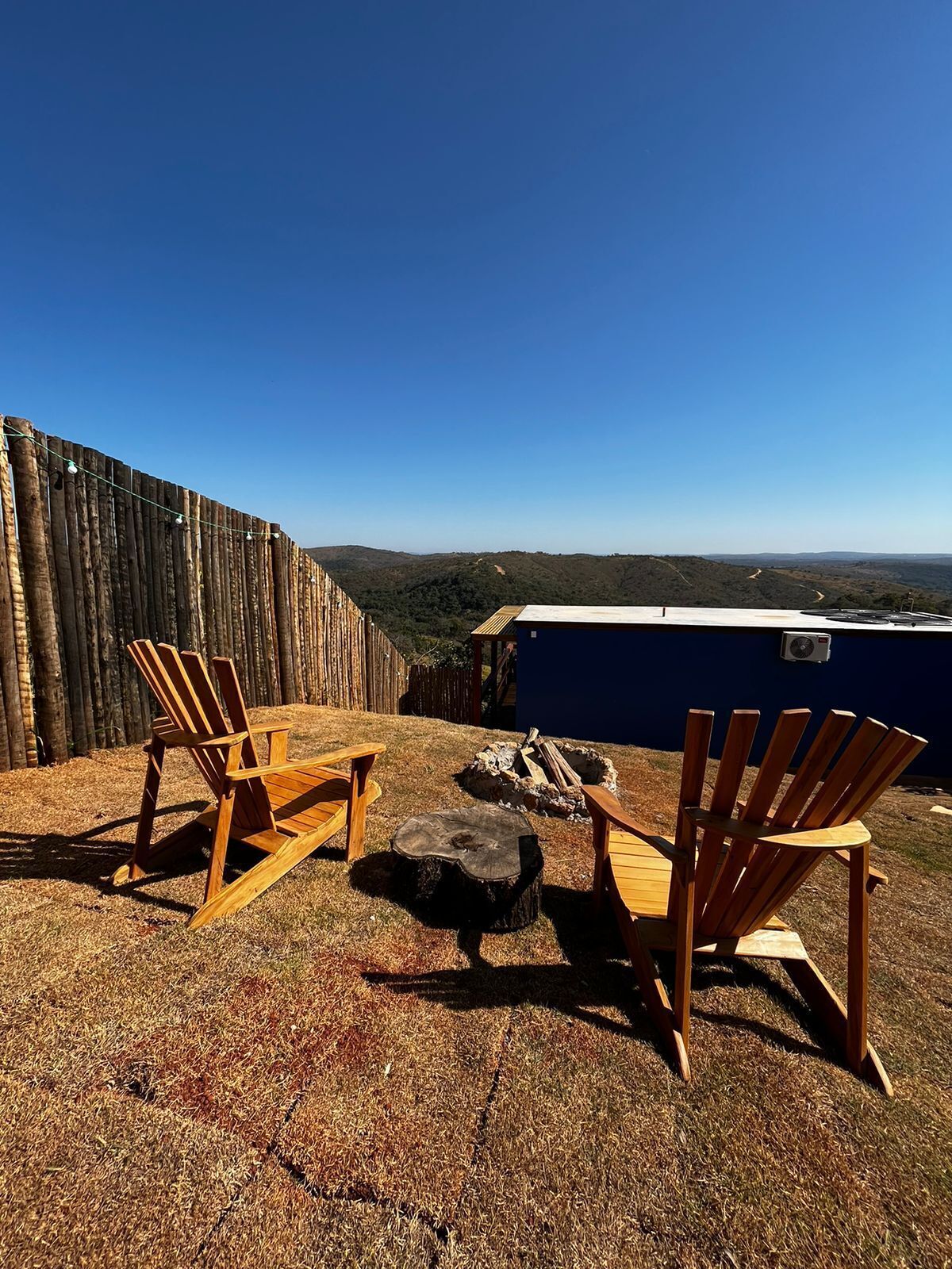 Un patio con due poltrone in legno di stile Adirondack, un braciere e vista su un paesaggio boschivo.
