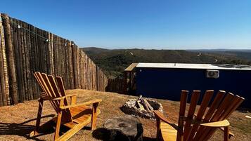 Un patio con due poltrone in legno di stile Adirondack, un braciere e vista su un paesaggio boschivo.
