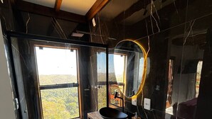 A modern bathroom with a large window, a black sink, and a wooden vanity.