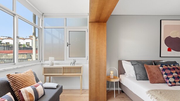 A modern bedroom with a sofa, a bed, a bedside table, and a window with a view of buildings. - GuestReady - Bright Studio in Bonfim District (Porto)