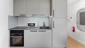 A compact kitchen with a microwave, oven, and sink. - GuestReady - Bright Studio in Bonfim District (Porto)