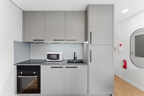 A compact kitchen with a microwave, oven, and sink. - GuestReady - Bright Studio in Bonfim District (Porto)