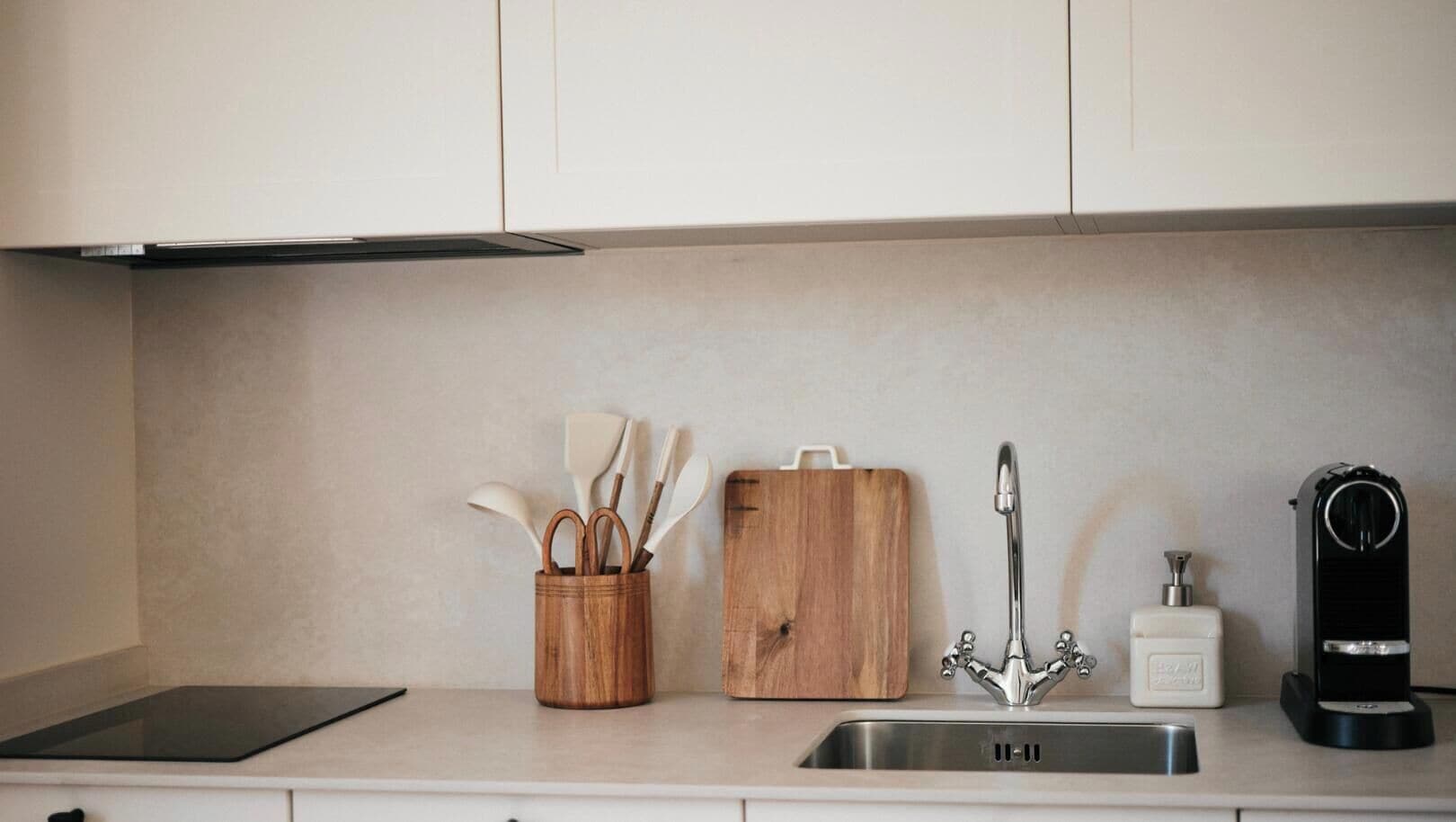 Een keuken met een roestvrijstalen spoelbak, een houten snijplank, een houten messenhouder en een koffieapparaat.