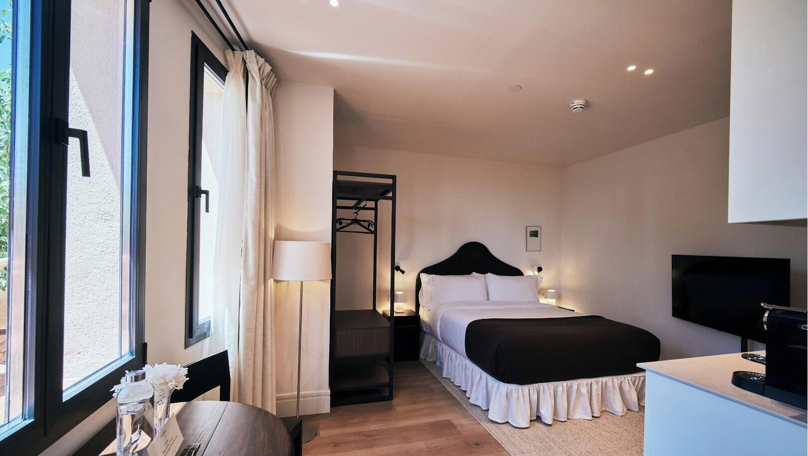 A hotel room with a bed, a television, a desk, and a window with curtains.