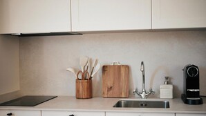 A kitchen with a stainless steel sink, a wooden cutting board, a wooden utensil holder, and a coffee machine.