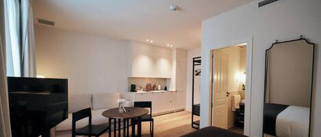 A hotel room with a bed, a small table with chairs, a kitchenette, and a bathroom.