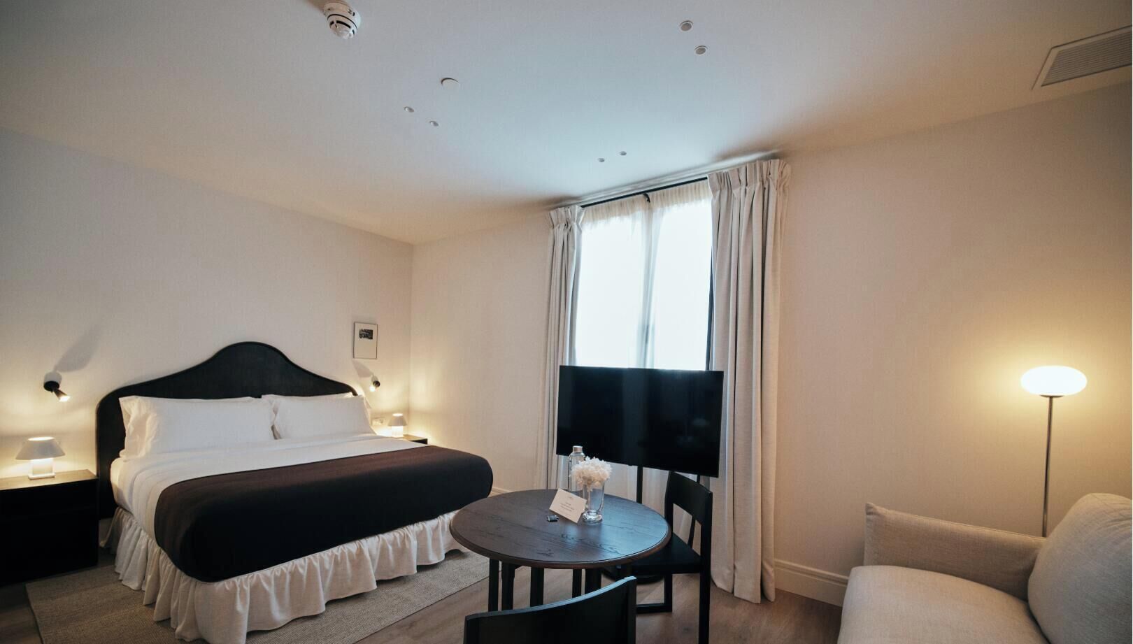 Habitación de hotel con cama, una mesa, una silla, televisor y lámpara.