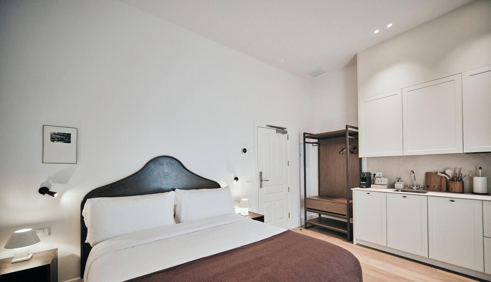 A modern bedroom with a bed, bedside table, and a nightstand. There is a wardrobe with a mirror and a door leading to a bathroom.