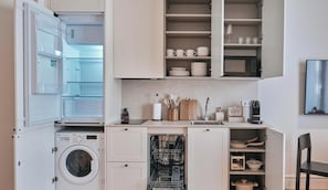 Une cuisine compacte équipée d’un lave-linge, d’un lave-vaisselle et de placards ouverts contenant de la vaisselle et des ustensiles.