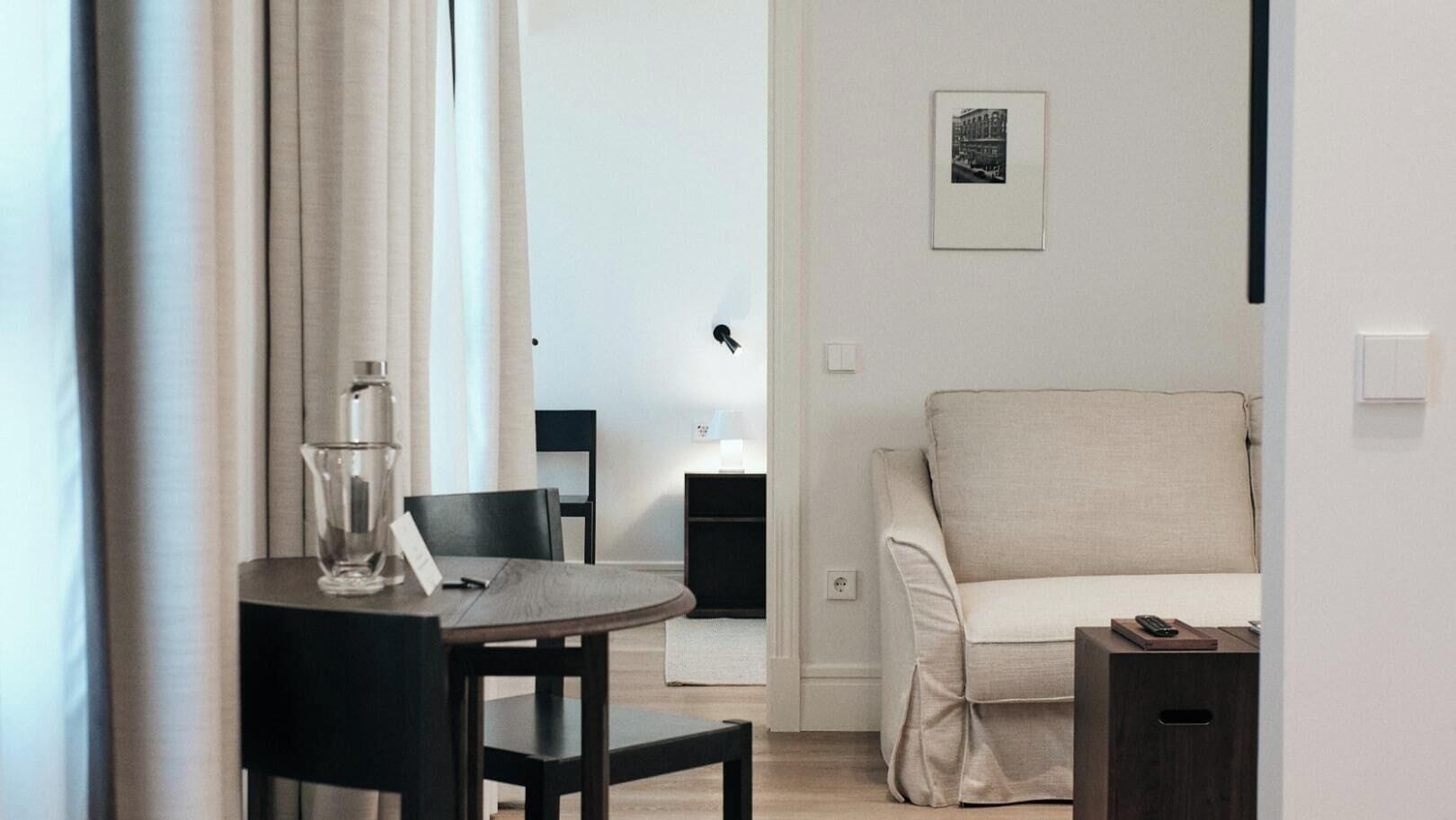 Een moderne hotelkamer met een ronde tafel, een bank, een klein kastje en een ingelijst schilderij aan de muur.