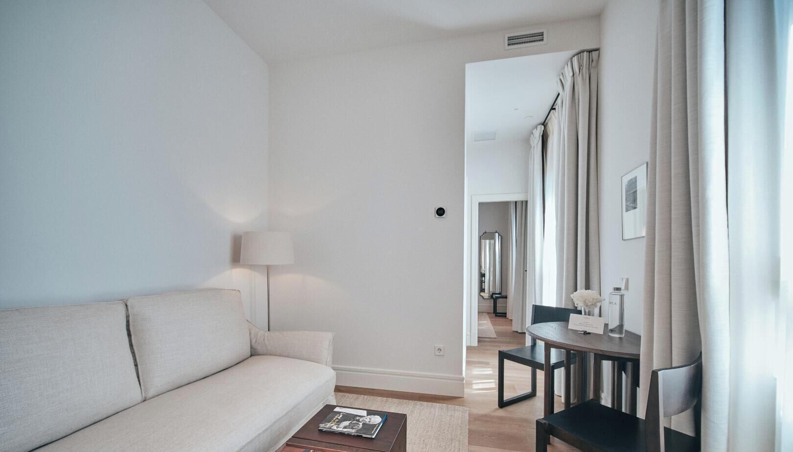 Ein modernes Wohnzimmer mit einer Couch, einem kleinen Tisch und einer Lampe. Ein Durchgang führt in einen Essbereich.