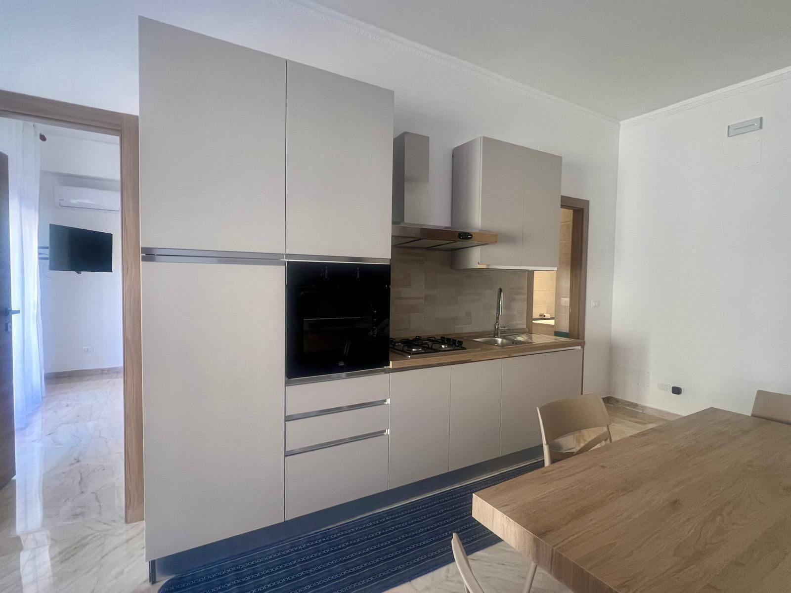 Una cucina moderna con elettrodomestici integrati, una zona pranzo con tavolo in legno e vista sullo spazio abitativo adiacente.