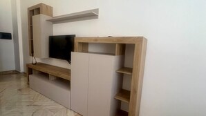 En modern möbel för underhållning med en platt-TV, trähyllor och ett golv med marmorliknande mönster.