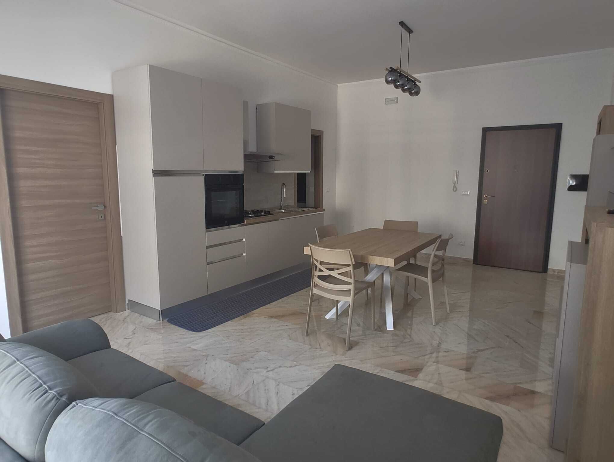 Una cucina moderna con elettrodomestici integrati, una zona pranzo con tavolo e sedie, e un divano grigio.