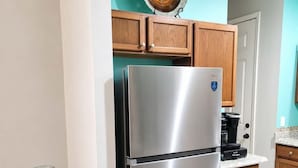 Una cocina con un refrigerador de acero inoxidable, armarios de madera, una pared de acento color turquesa y un florero de vidrio transparente.