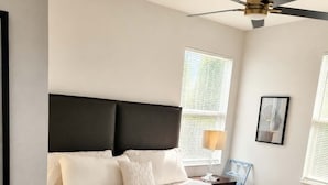 Un dormitorio con una cama grande, un ventilador de techo y una mesita de noche con lámpara.