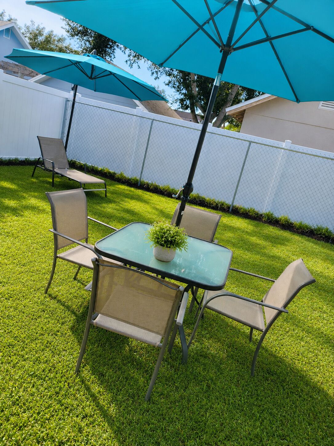 Een terras met een tafel, stoelen, een bloempot en een blauwe parasol.