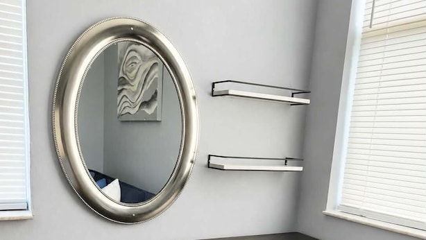 Una habitación con pared gris, un espejo redondo, una mesa negra con patas metálicas y un taburete azul con un diseño geométrico.