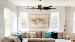 Una sala de estar con un sofá modular, una mesa de centro de vidrio y un ventilador de techo.