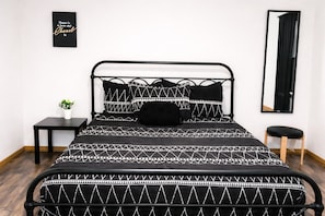 Un lit avec un cadre en métal noir, une literie à motifs noir et blanc, une petite table de chevet avec une plante et un miroir accroché au mur.