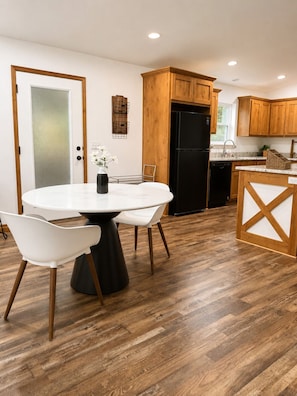 Eine moderne Küche mit Holzausstattung, einem schwarzen Kühlschrank und einem Essbereich mit rundem Tisch und weißen Stühlen.