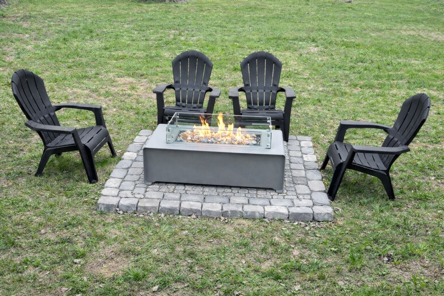 Un foyer extérieur carré, entouré de quatre chaises Adirondack noires, le tout posé sur une base en pierre.