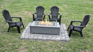 Un foyer extérieur carré, entouré de quatre chaises Adirondack noires, le tout posé sur une base en pierre.