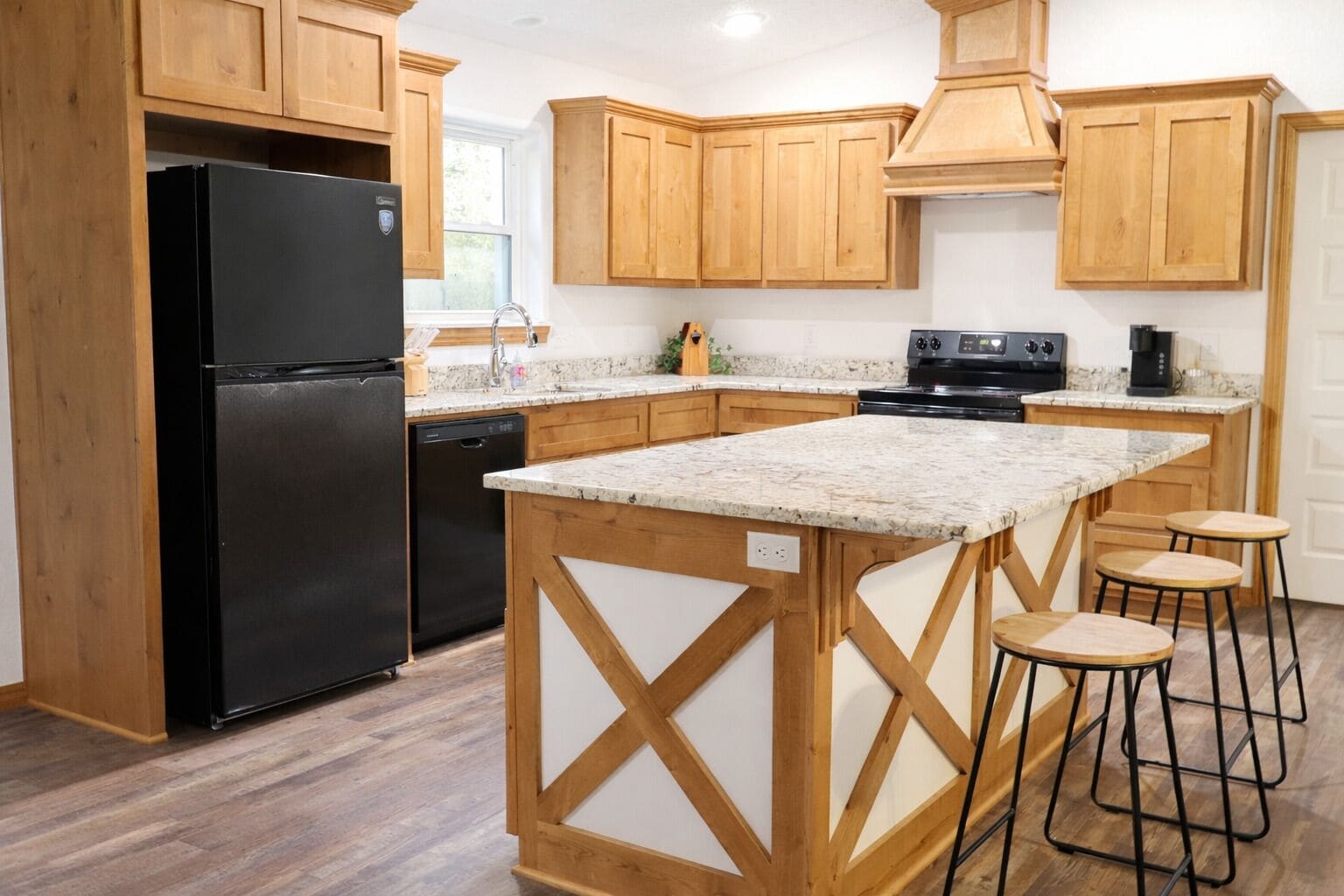 A kitchen with wooden cabinets, a black refrigerator, a granite countertop, and a bar stool area.