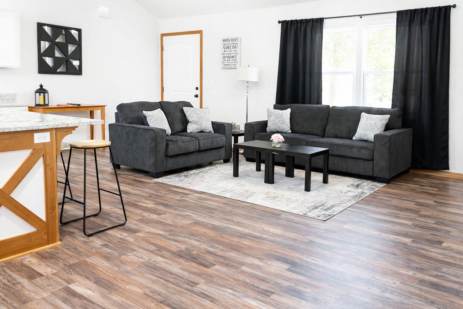 Un salon moderne avec un canapé gris, une table basse et une table à manger en bois, ainsi que des tabourets de bar.