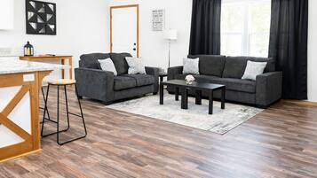 Un salon moderne avec un canapé gris, une table basse et une table à manger en bois, ainsi que des tabourets de bar.