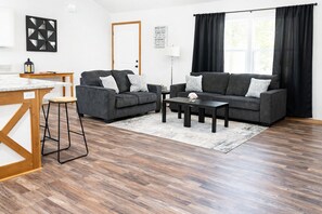 Ein modernes Wohnzimmer mit einem grauen Sofagarnitur, einem Couchtisch und einem Holzessttisch mit Barhocker.