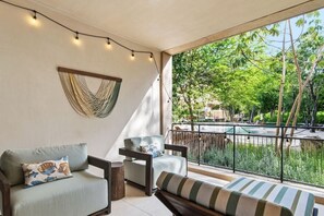 A balcony with a sofa, armchair, and striped bench, overlooking a pool and greenery. - Yáax K'iin: Poolside Oasis + Free E-Bikes (Playa del Carmen)