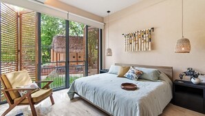 Ein Schlafzimmer mit einem großen Bett, einem Sessel, einem Nachttisch und Blick ins Freie.