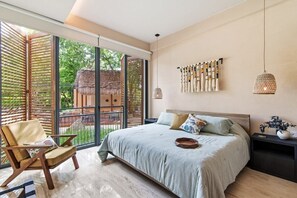 A bedroom with a large bed, a chair, a nightstand, and a view of the outside. - Yáax K'iin: Poolside Oasis + Free E-Bikes (Playa del Carmen)