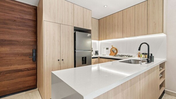 Eine moderne Küche mit Holzausstattung, einem Edelstahlkühlschrank, einer weißen Arbeitsplatte und einem schwarzen Wasserhahn.