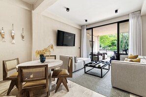 A modern living room with a dining area, a flat-screen TV mounted on the wall, and a large sliding glass door leading to an outdoor area. - Yáax K'iin: Poolside Oasis + Free E-Bikes (Playa del Carmen)