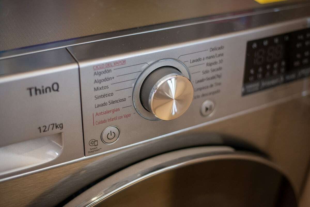 A front-loading washing machine with a control panel featuring a knob and various washing options.