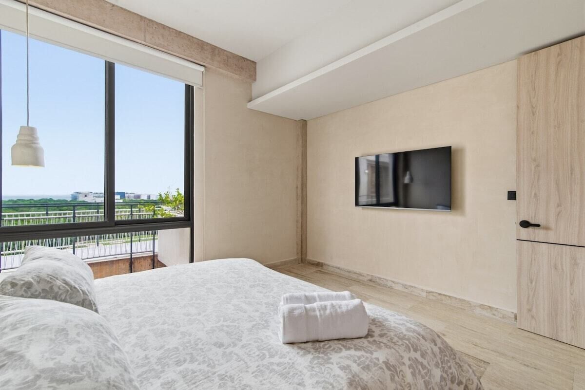 Ein Schlafzimmer mit großem Fenster, einem Bett, einem Flachbildfernseher und einem Kleiderschrank.