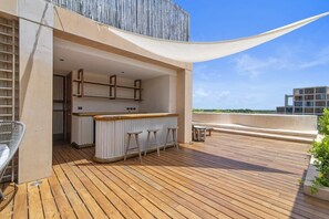 A wooden deck with a bar area, bar stools, and a chair. - Túumben: Penthouse Unit w/ Spectacular Ocean & Golf Views (Playa del Carmen)