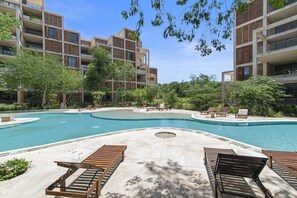 A modern building with a pool, lounge chairs, and greenery. - Túumben: Penthouse Unit w/ Spectacular Ocean & Golf Views (Playa del Carmen)