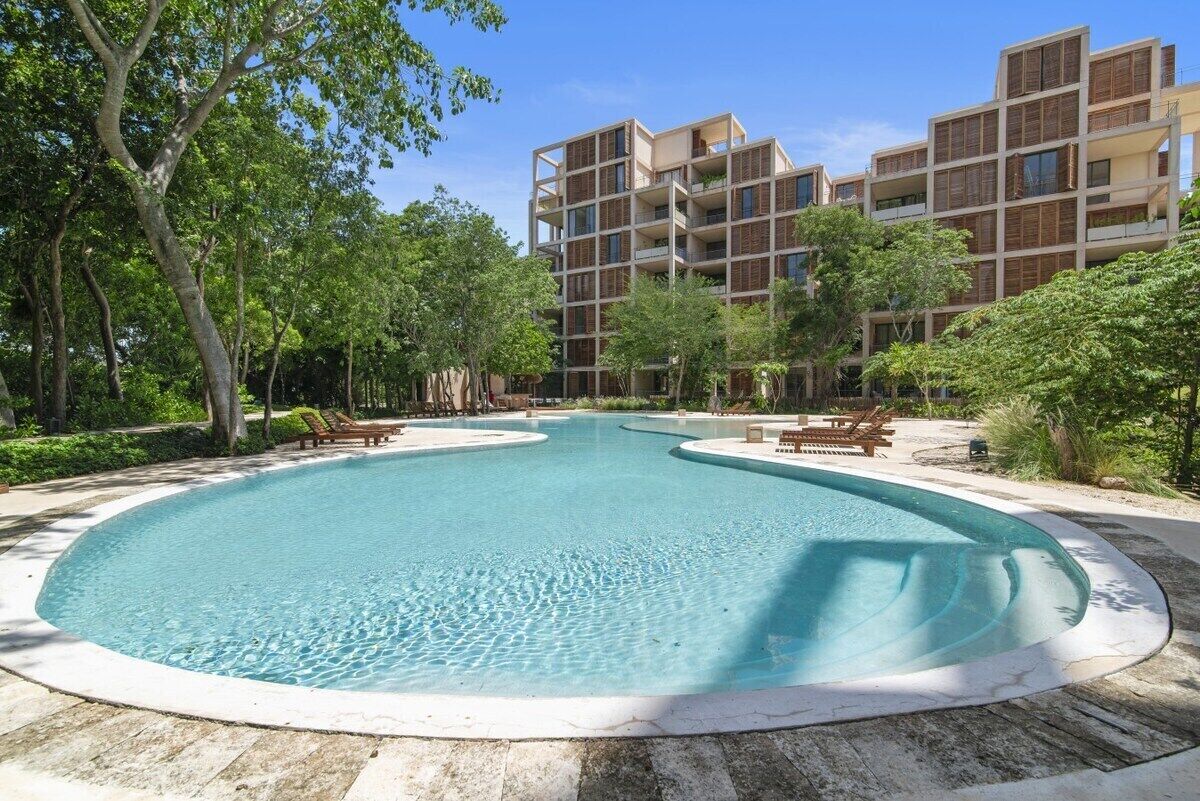 Una piscina rodeada de sillas de descanso y un edificio de varios pisos con balcones.